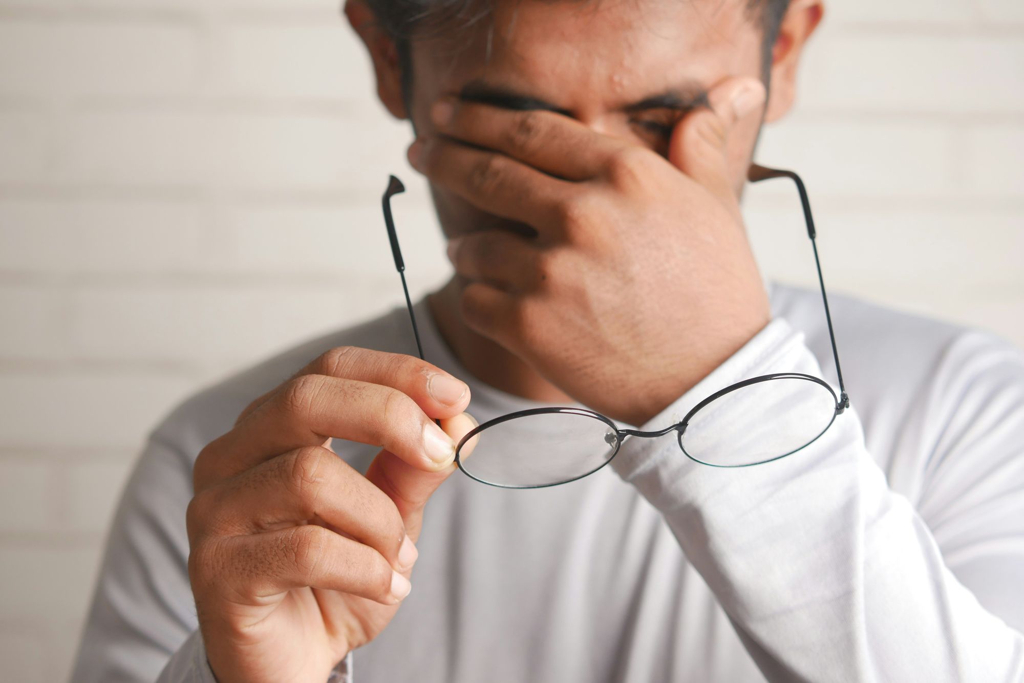Man rubbing his eyes with glasses in his hand