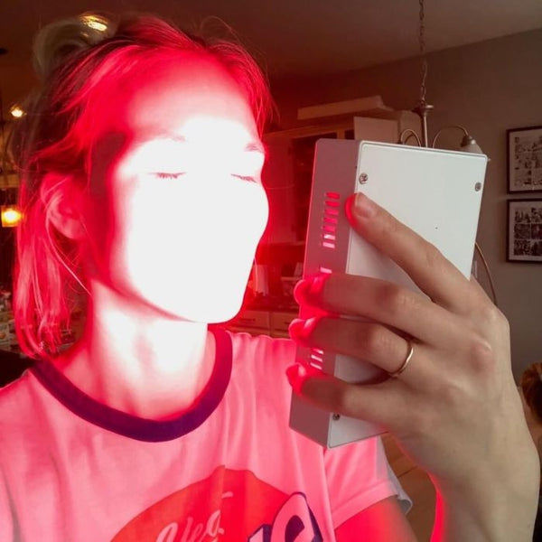 A woman treating her face with red light therapy.