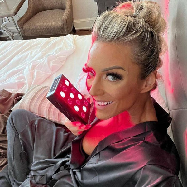Woman relaxing with a handheld KOZE Mini Red Light Therapy device, highlighting its convenience for skin and health treatment.