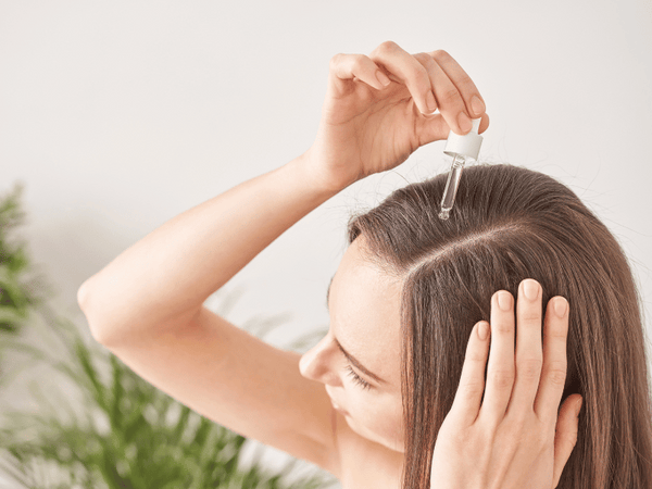 an image of a woman dropping hair supplements on her hair using a tincture.