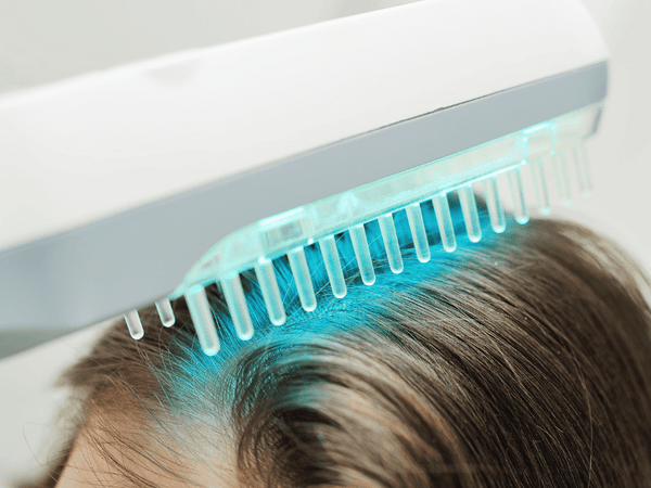 an image of a woman using a handheld ultraviolet device on her scalp