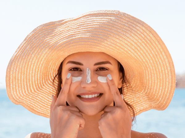 An image of a woman applying sunscreen on her face.