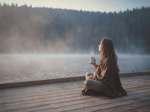a woman watching the sunrise, sitting at the backyard deck while drinking coffee.