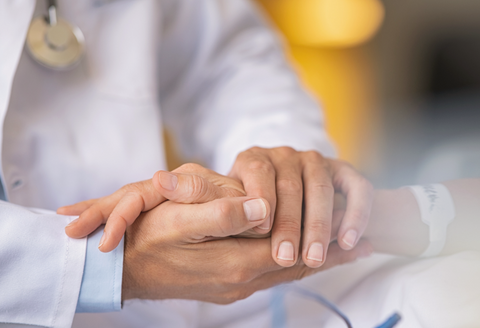 A close up of a doctor holding a woman's hand reassuringly