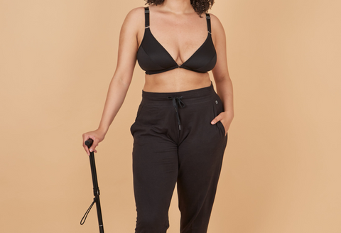 Woman from the neck down wearing Springrose's limited mobility bra in black and black joggers while leaning on a cane