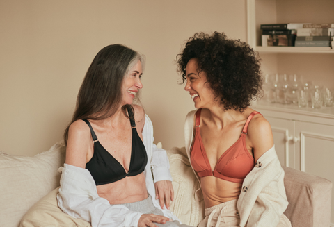 Two beautiful older women looking at each other and laughing while lounging on the couch in their Springrose limited mobility bras