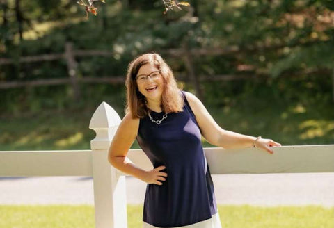 Morgan in a blue dress, laughing as she's leaning against a white picket fence