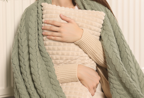 Gifts for patients with brain tumors: heated pillows. A woman wrapped in a green blanket has her arms wrapped around a pillow.