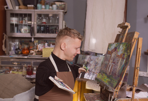 Man with two limb differences painting a beautiful, scenic piece on a canvas