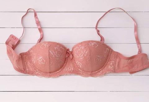 Can bra cause back pain: a pretty lacey, pink wired bra laying on top of white shiplap