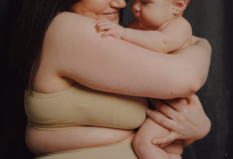 Why is postpartum care important: a close up of a woman as she holds her baby. You can only see from the waist to her nose.