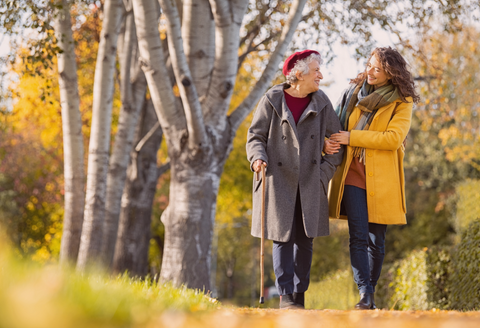 Two women of different generations walking with arms linked through a park during an autumn day