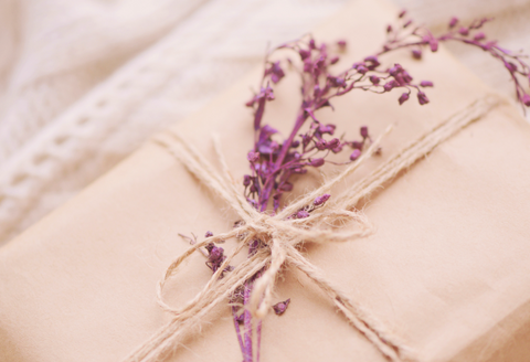 A neutral colored gift wrapped box tied with string and a sprig of lavander