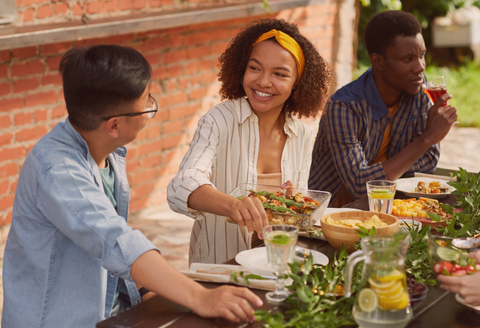 Three young people talking and smiling around a table with food