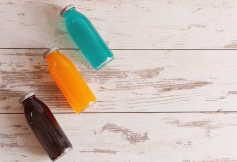 Ehlers Danlos Syndrome Gifts: three bottles with brightly colored liquid on a wood table, signifying an electrolyte drink