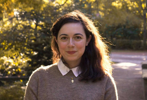 Britt, a pretty young woman, smiling a bit while staring at the camera in a scholarly-looking outfit