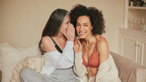 Two beautiful women sharing a secret while wearing their Springrose adaptive bra and sitting on the couch