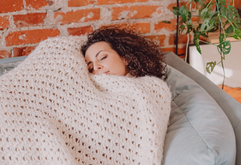 ehlers danlos menstruation: woman napping on a couch with a big comfy blanket on top