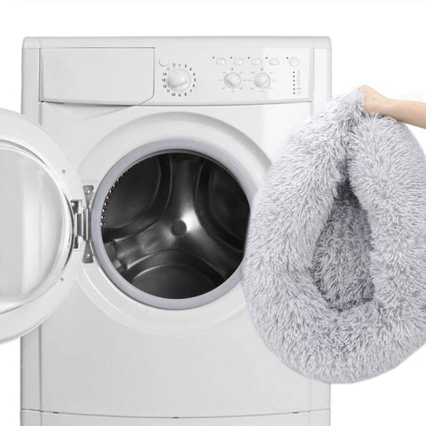 A hand putting a light gray Calming Cuddle Bed into a washing machine