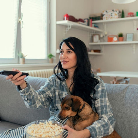 A puppy cuddling its human on the couch looking at a bowl of popcorn