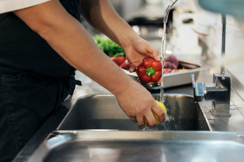 Male chef washing peppers under tap before cooking them
