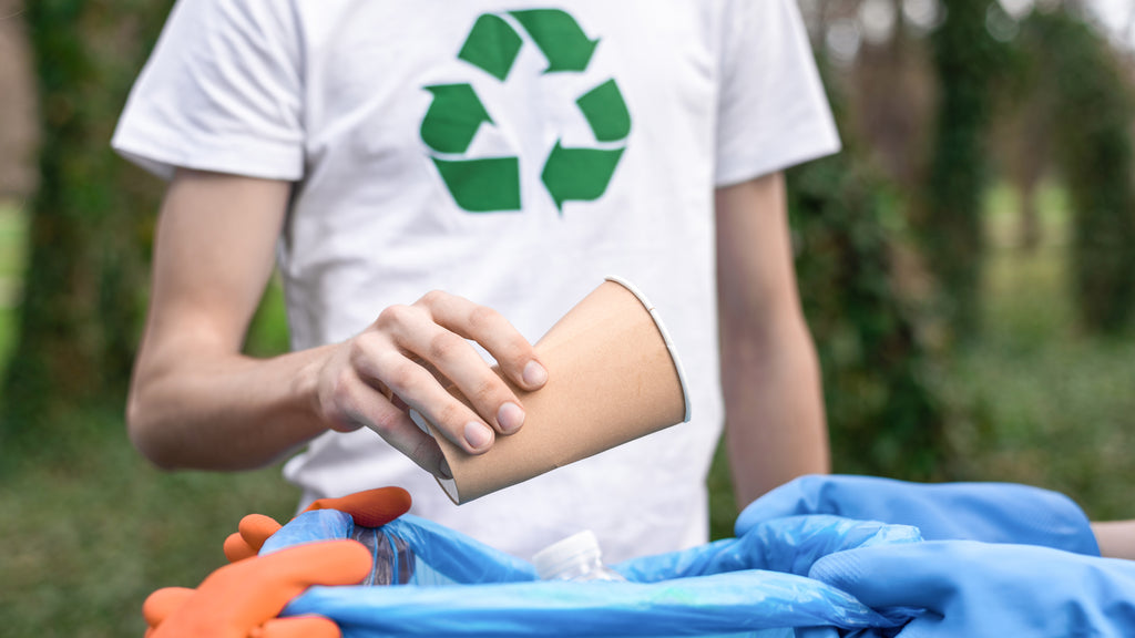 man with recycling logo on shirt disposing of sustainable coffee cup