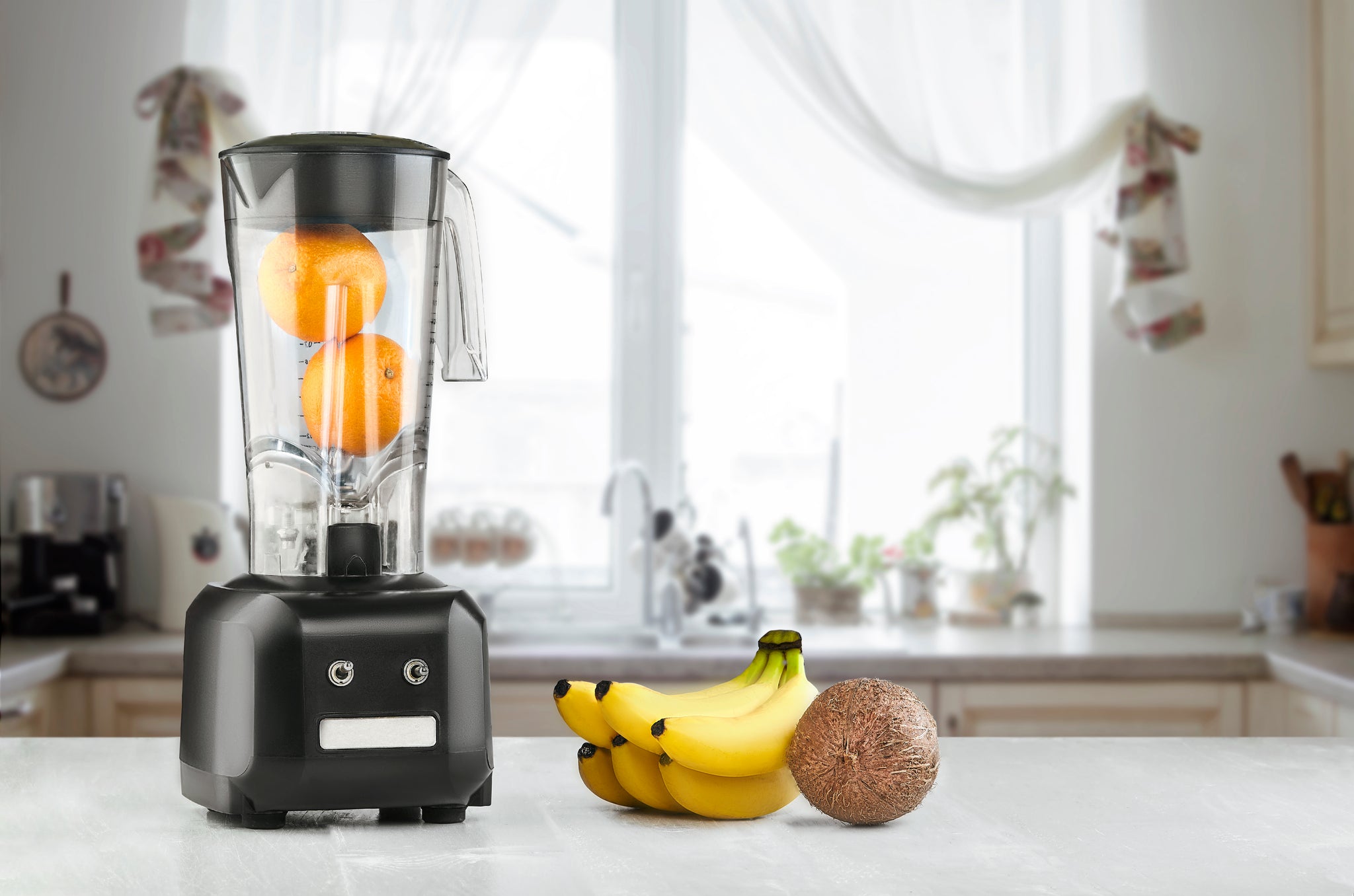 Metal blender with oranges inside and bananas to the side