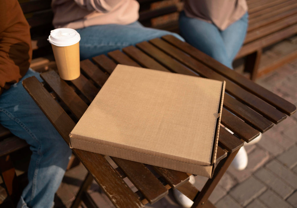 Square pizza box on table next to takeaway coffee cup