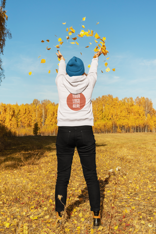 woman wearing a white hoodie throwing autumn leaves in the air