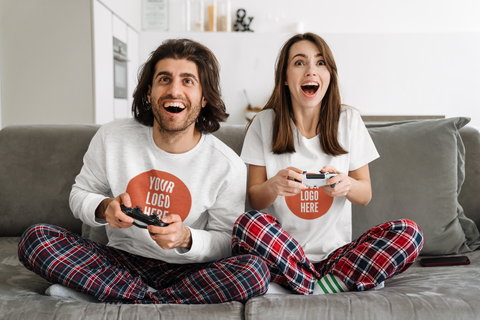 a man and woman wearing a sweatshirt and t shirt playing video games on a couch