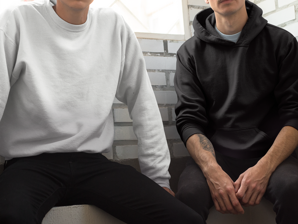 Two men sitting chatting, wearing hoodies. One in white and other in black. The image does not show the men's faces