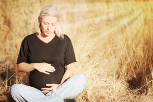 Snugglebundl - Baby Brain Blog - An Image of a women sitting cross leg in a field hugging her baby bump