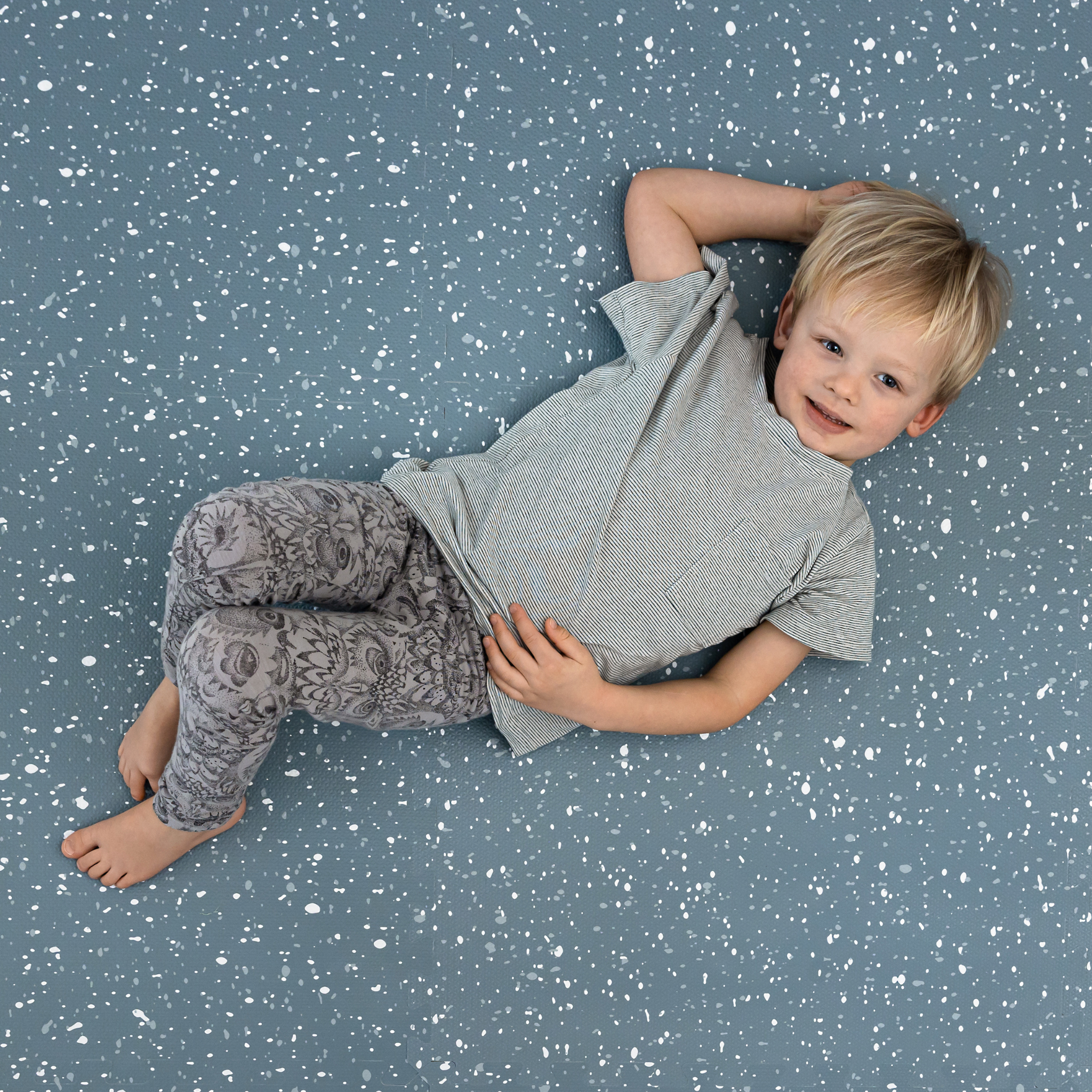 A smiling young child lying on a speckled blue background.