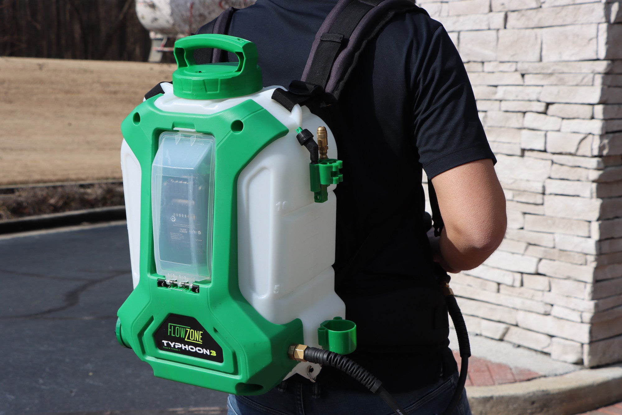 man with typhoon 3 battery sprayer on his back facing brick column