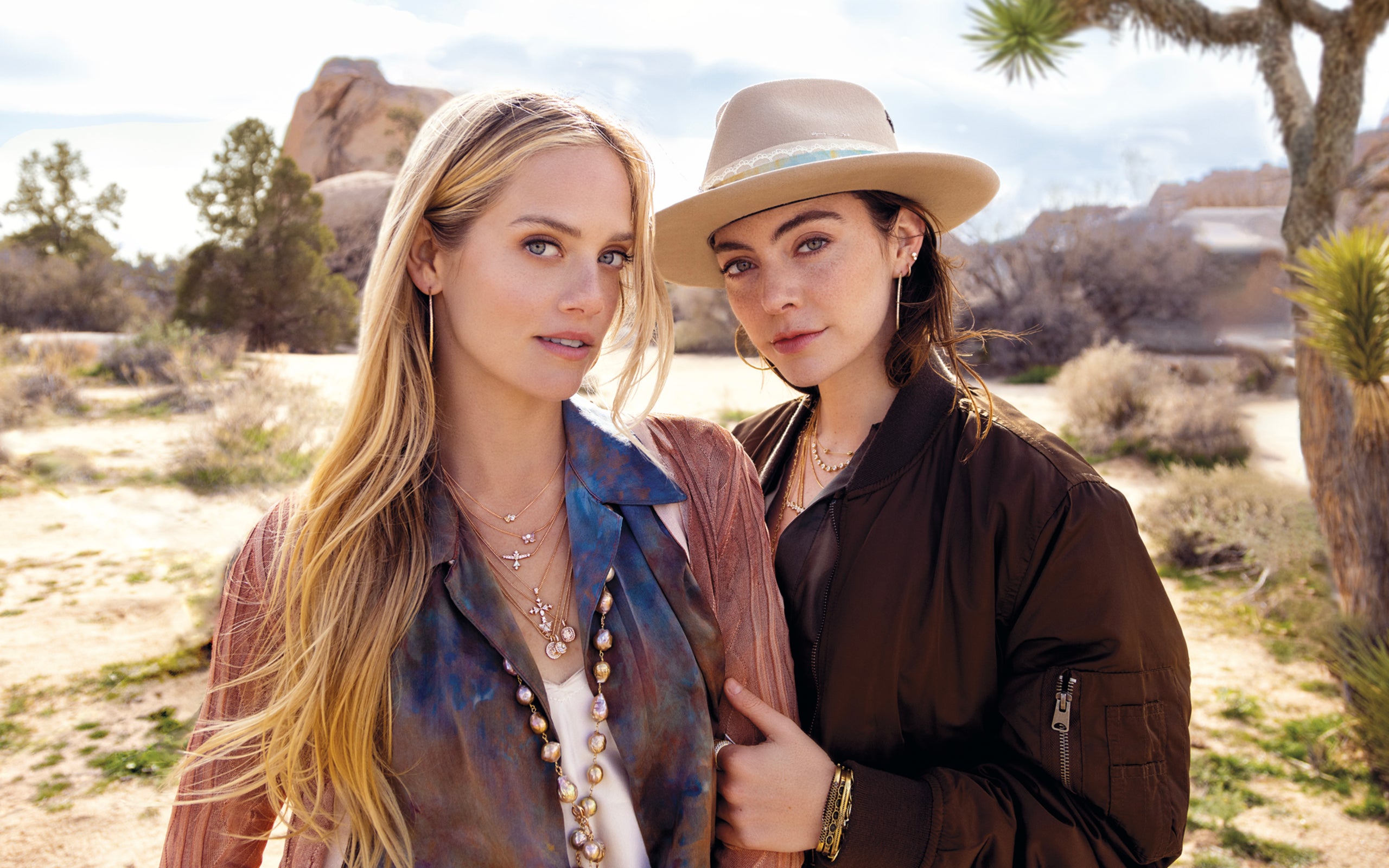 Arm in arm women wearing California lifestyle designer diamond jewelry, hats, silk apparel while standing in desert; phone, text 323-404-2959 for shopping help.