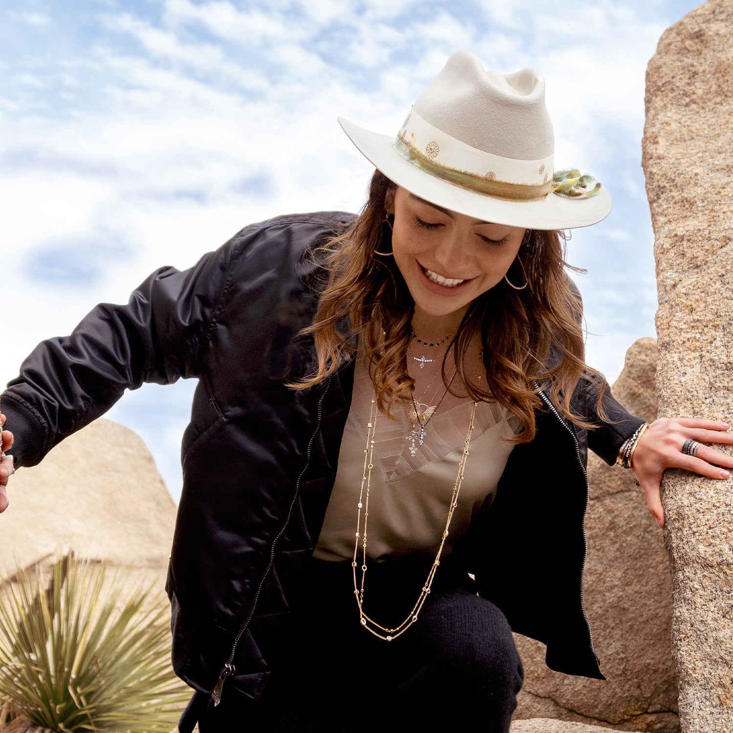 Woman wearing Dominique Cohen limited edition hat, pink diamond, white diamond rose gold, black gold stylish jewelry and bomber jacket while hiking; phone 323-404-2959 for shopping help.