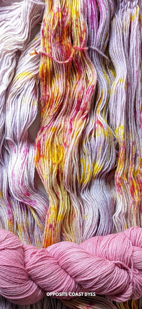 background: pink based yarn with yellow streaks and magenta speckles spread out. foreground: skein of bright pink yarn