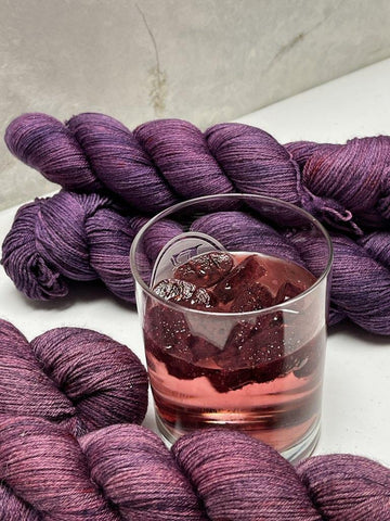 glass of seltzer with berry ice surrounded by purple yarn