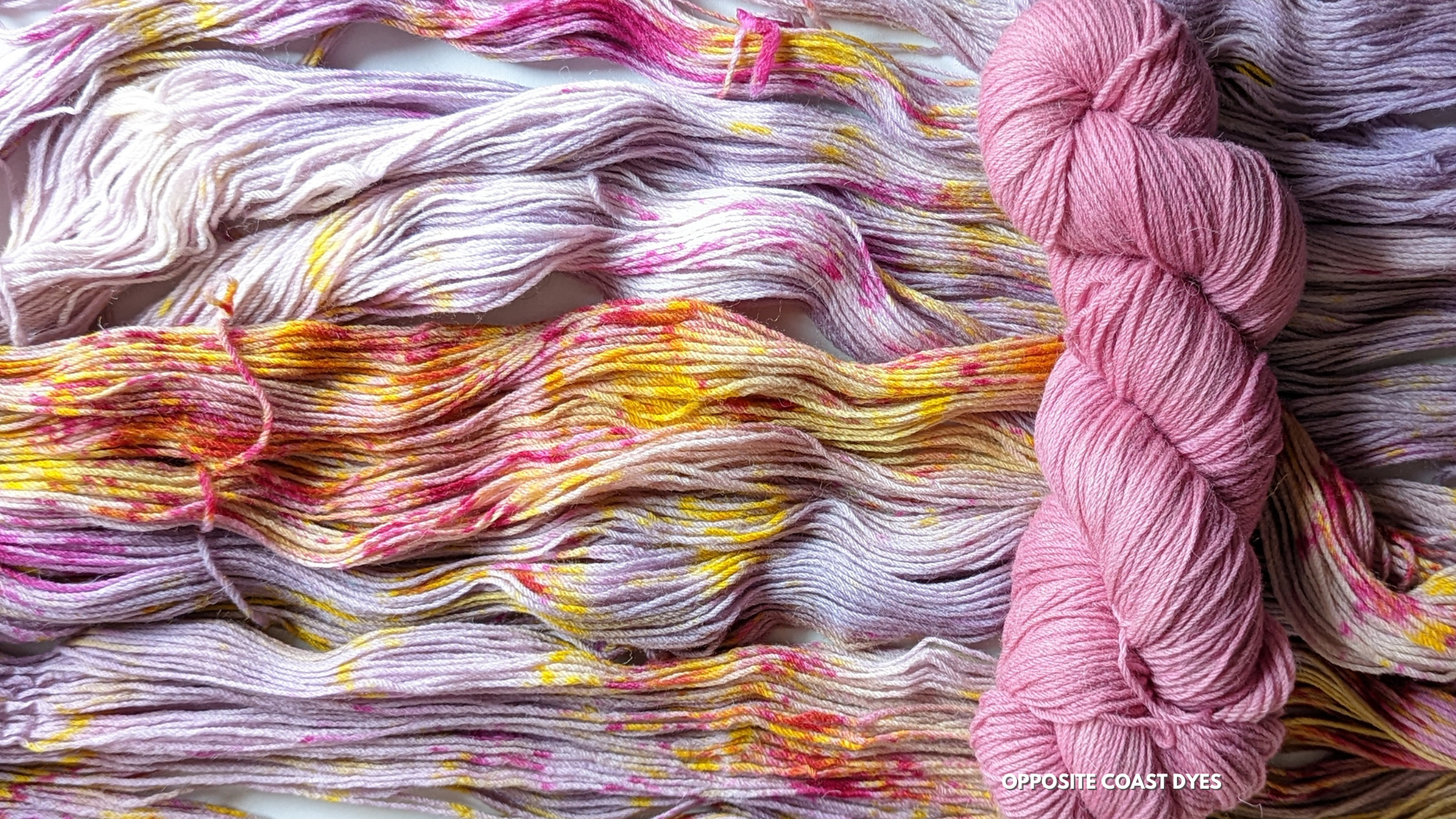 background: pink based yarn with yellow streaks and magenta speckles spread out. foreground: skein of bright pink yarn