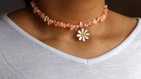 Un collier choker en perles nuggets roses avec un charm en forme de marguerite au milieu met en valeur un cou