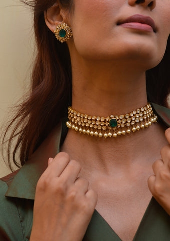 Une femme porte un ras de cou serti de perles avec une émeraude au milieu.