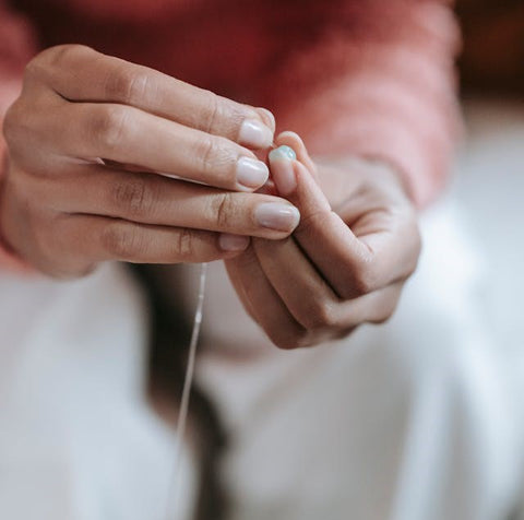 Gros plan sur les mains d'une femme en train d'enfiler un fil élastique à travers le trou d'une perle naturelle.