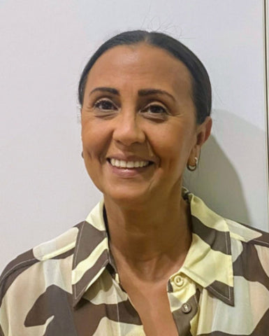 Close up of woman smiling on a blank wall. She is wearing a brown and white shirt
