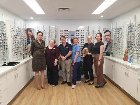 People standing in an optometrist shop surrounded by displays of glasses.