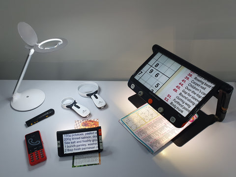 Daily living aids displayed on a desk including magnifiers, phone and light
