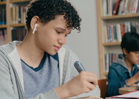 Boy sitting in library with an ear bud using OrCam Learn