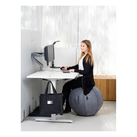 Nainen istuu aktiivipallon päällä työpöydän ääressä