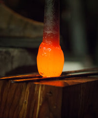 The radiant orange glow of molten glass at the end of a blowpipe, captured in the dark ambiance of a glassblowing studio, showcases the intense heat and malleability during the glass shaping process.