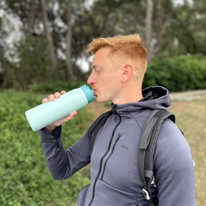 Man drinking water from a blue bottle outdoors with a backpack on.