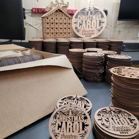 Multiple wooden ornaments laser-cut with Theatre Calgary's logo by LightBurnDesign.